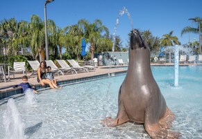 Un área de piscina con sillas de descanso, una estatua de delfín y un cielo azul despejado.