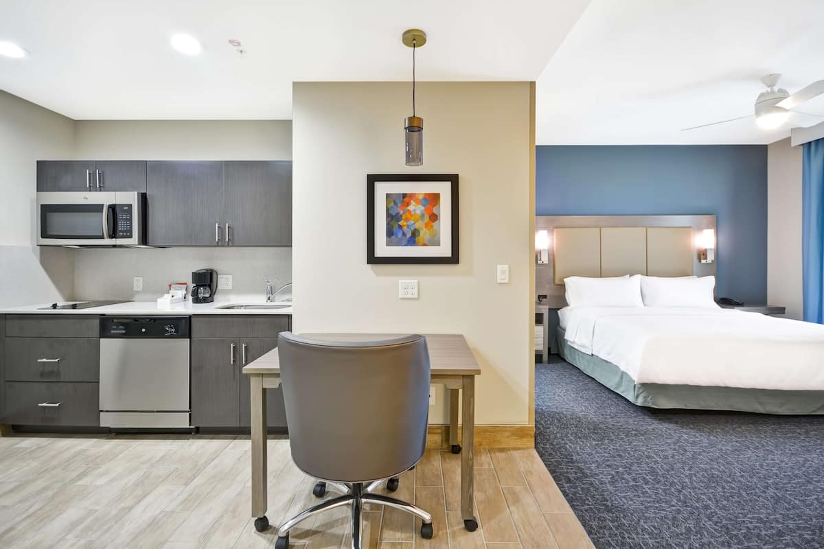 Habitación de hotel con cama, escritorio, silla, microondas, cafetera y lavavajillas.