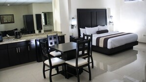 A hotel room with a bed, a desk, chairs, a kitchen area, and a large mirror. - Hotel El Camino Inn & Suites (Reynosa)