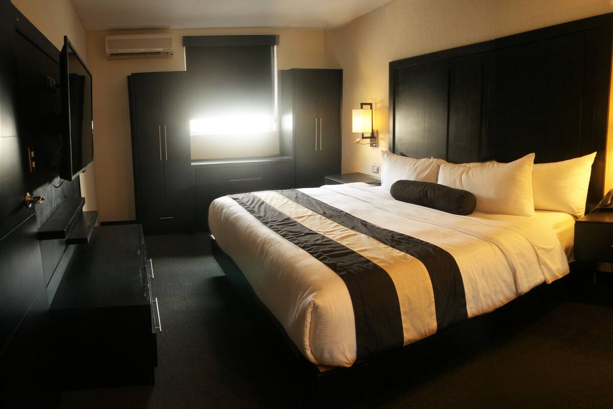 A hotel room with a large bed, bedside tables, a TV, and a window with blinds.