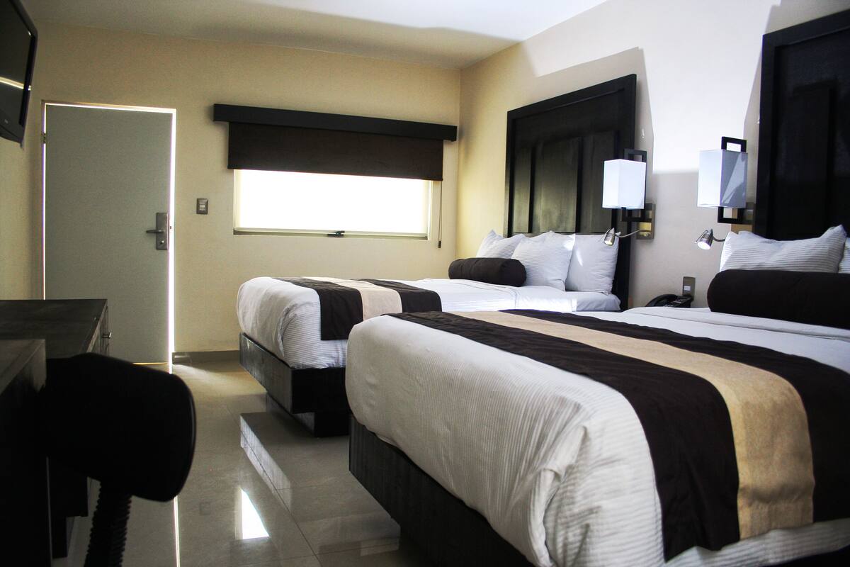 A hotel room with two beds, a desk, and a chair.
