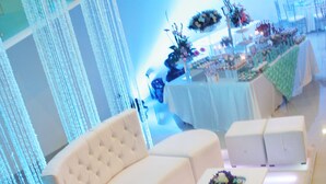 A modern lounge area with a white sofa, a coffee table with a floral arrangement, and a dining area in the background with tables and chairs. - Hotel El Camino Inn & Suites (Reynosa)