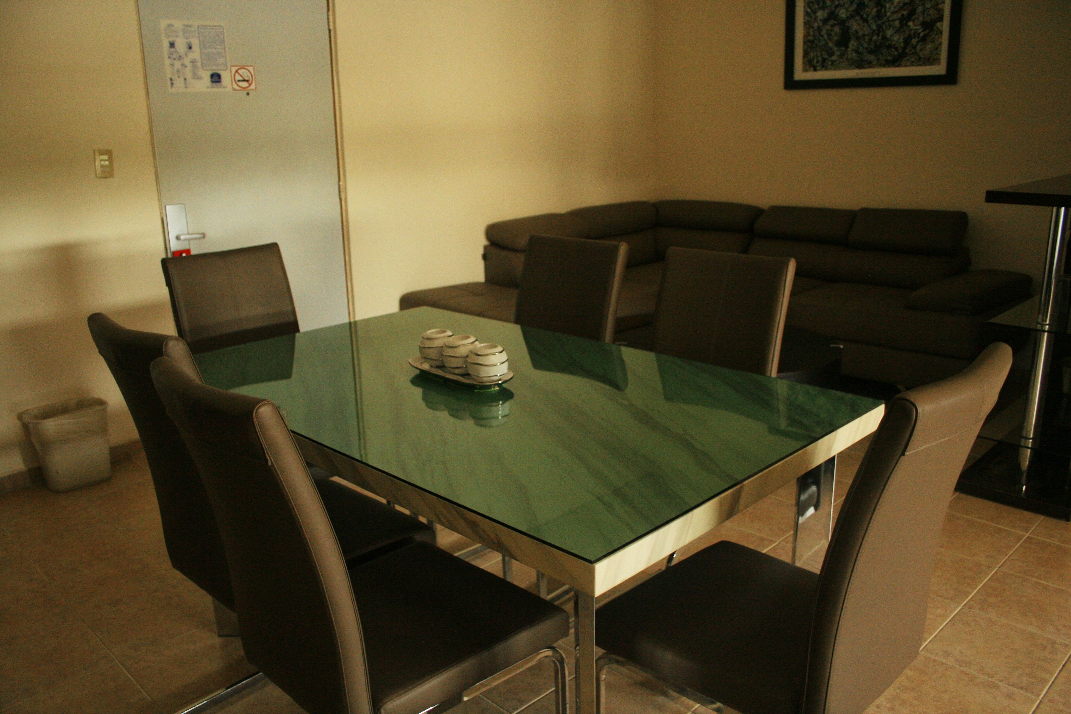 A dining area with a glass table, four chairs, and a brown sofa.