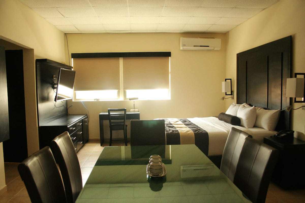 A hotel room with a bed, a desk, a chair, a TV, and a window.