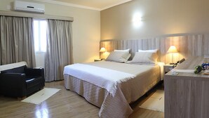 Een hotelkamer met een groot bed, twee nachtkastjes met lampen, een bureau, een stoel en een airconditioner.