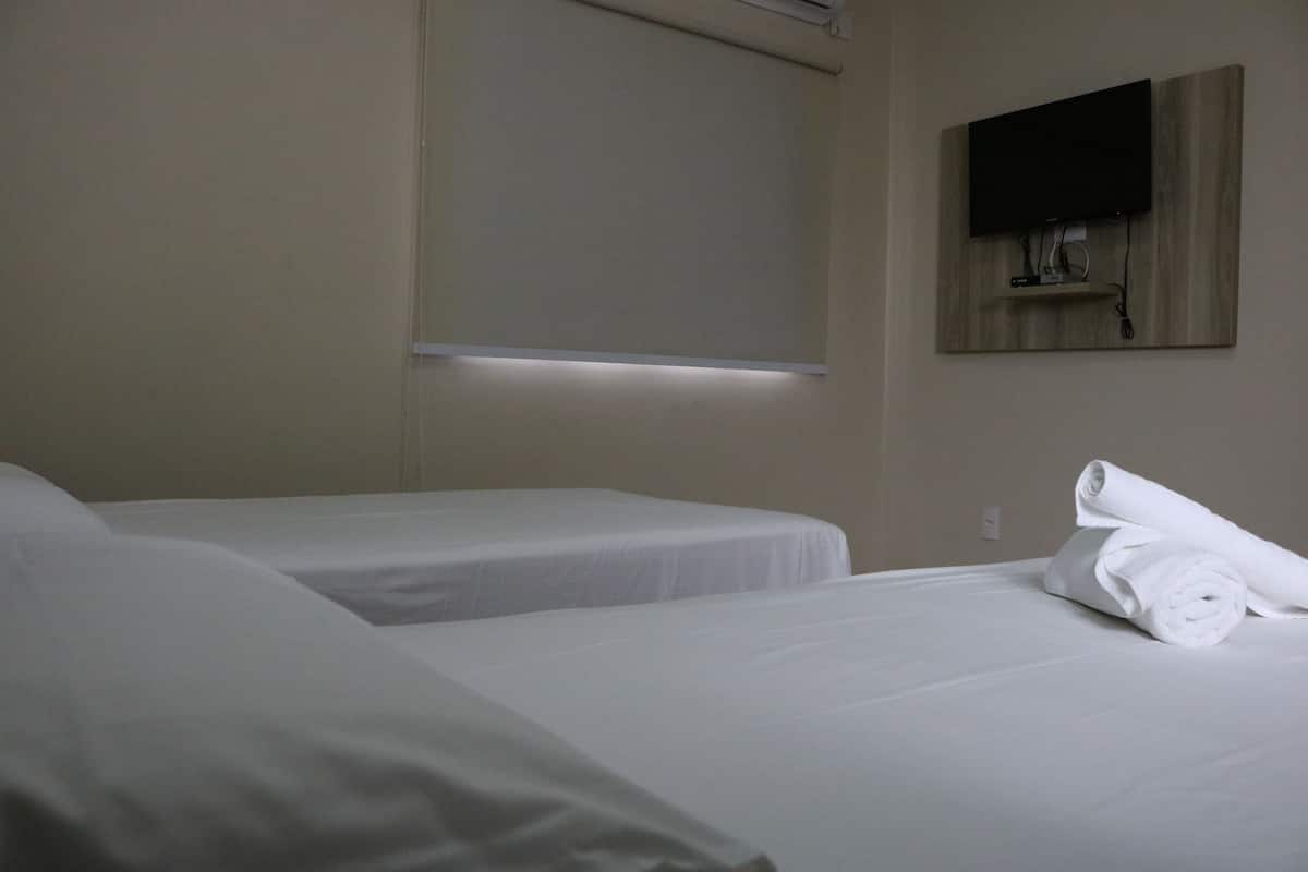 A hotel room with two beds, a flat-screen TV mounted on the wall, and a neatly rolled towel on the bed.