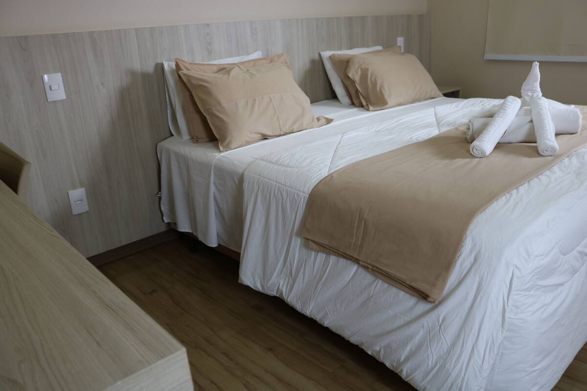 A hotel room with two beds, beige bedding, and a wooden floor.