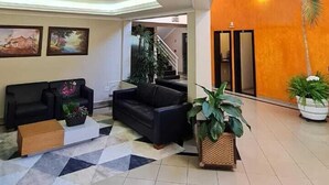 Een ruime lobby met een hoge plafond, een trap en een zithoek met banken en potplanten.