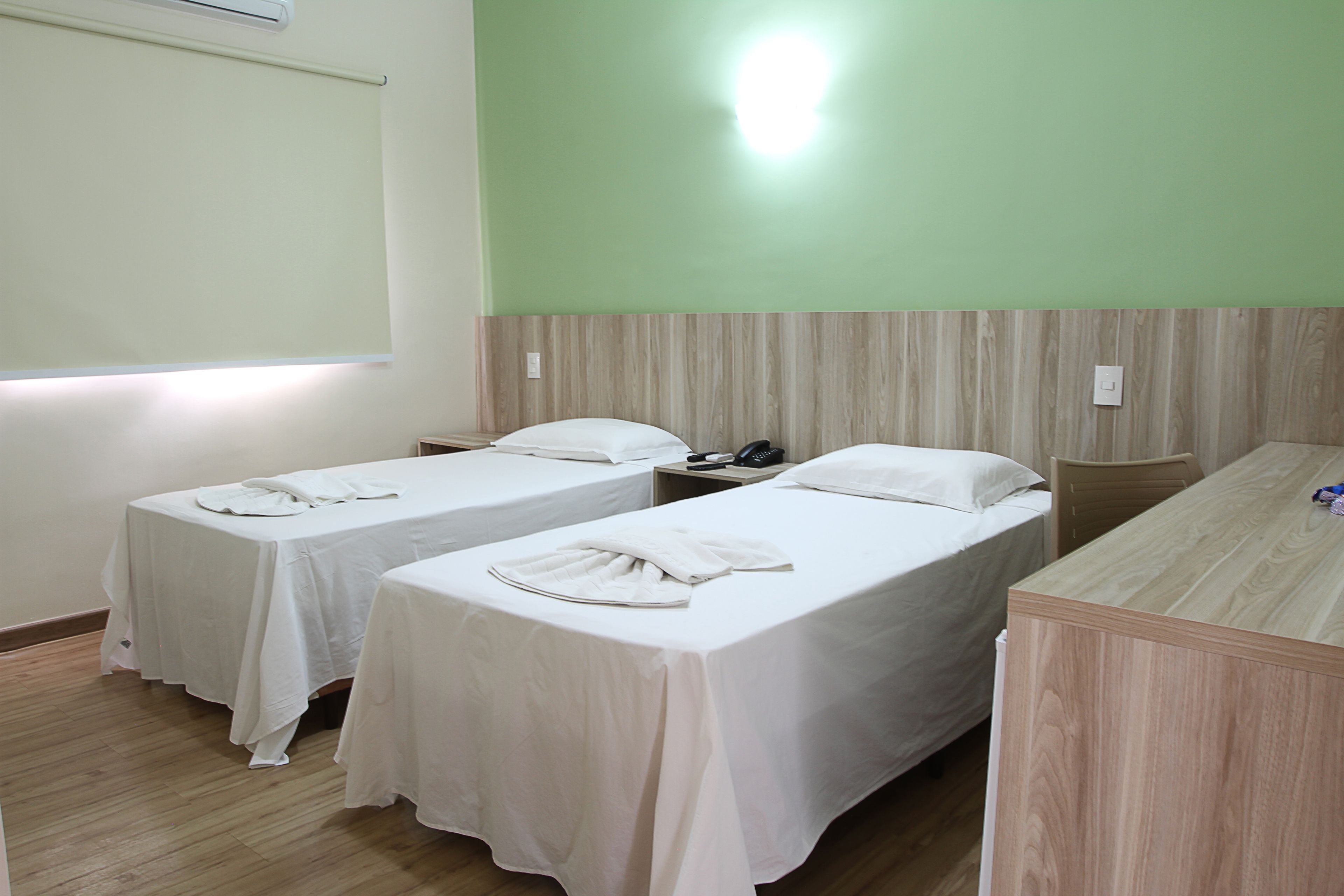 Habitación de hotel con dos camas individuales, un escritorio de madera, un teléfono y una lámpara de pared.