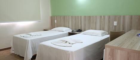 A hotel room with two single beds, a wooden desk, a telephone, and a wall-mounted light.
