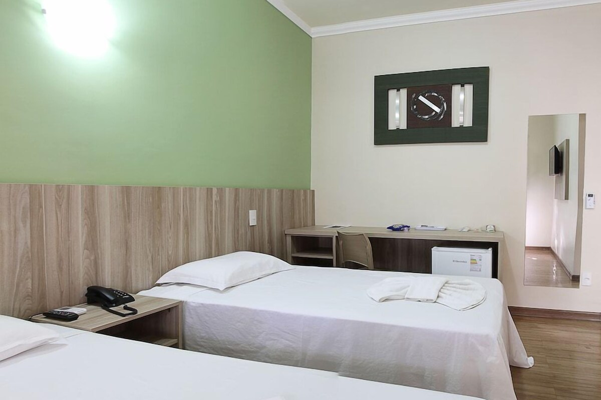A hotel room with two beds, a desk, a clock, and a mirror.