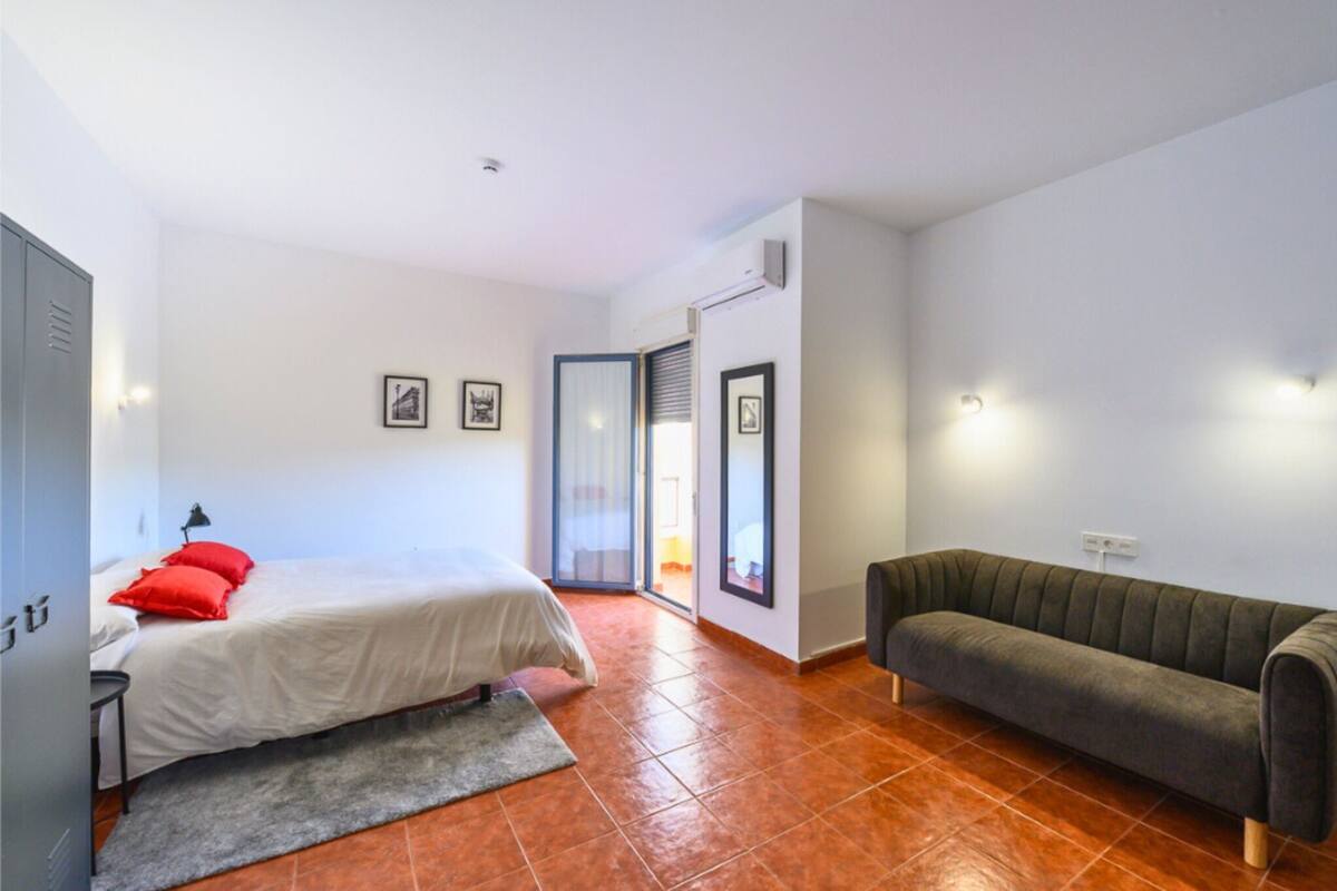 A bedroom with a bed, a sofa, a wardrobe, and a sliding glass door leading to a balcony.