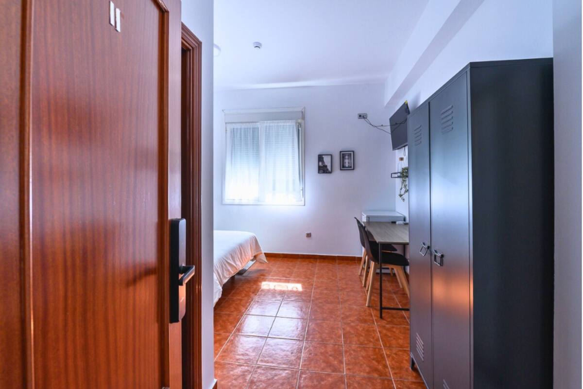 A room with a bed, a desk, a wardrobe, and a window with curtains.