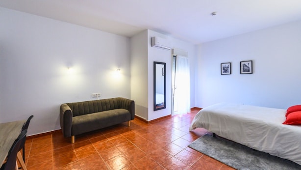 A room with a bed, a sofa, a chair, a small table, and a door leading to another room. - Hotel Lazkao  (Lazkao)