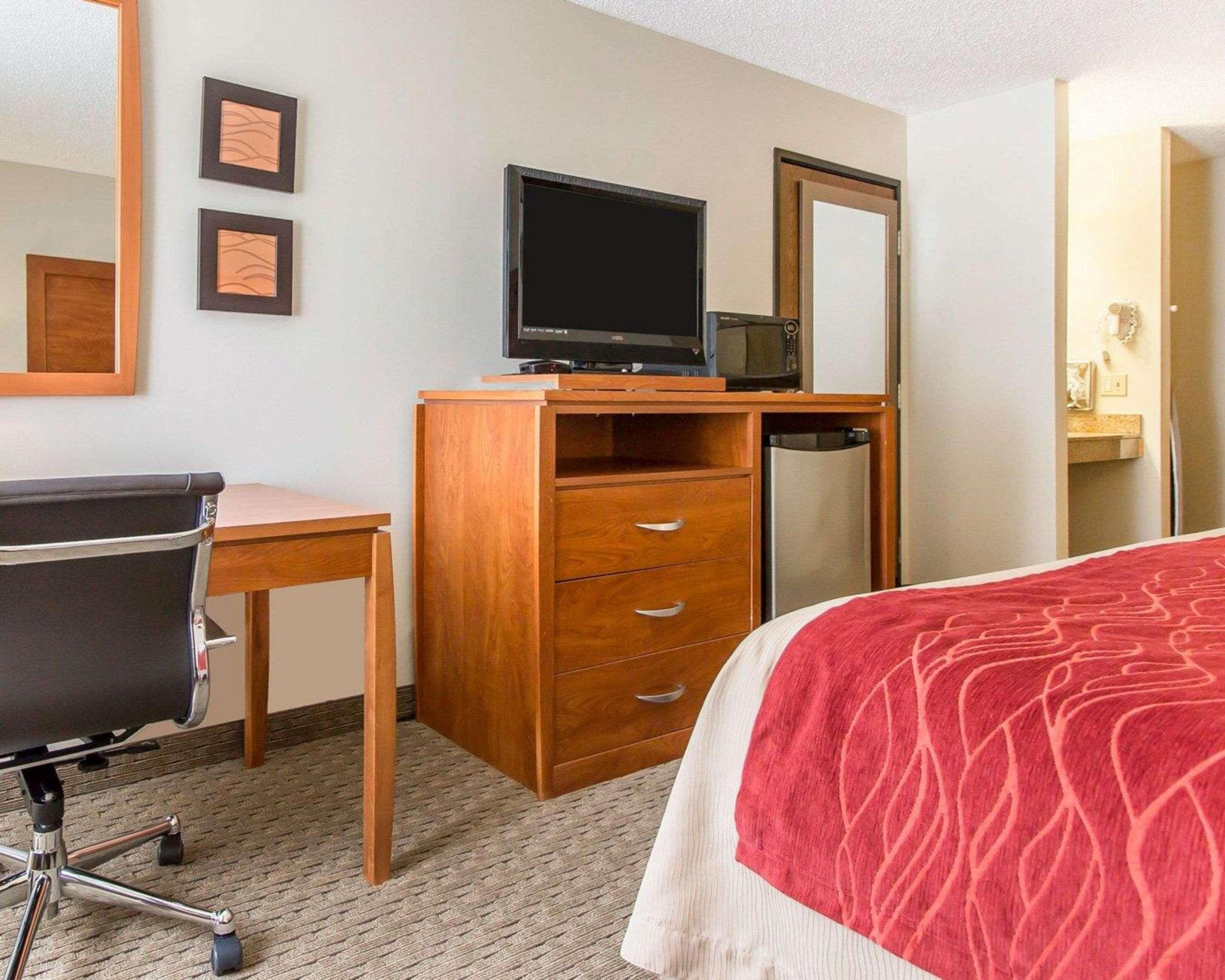 Una habitación de hotel con una cama, un escritorio con silla, televisión y microondas.