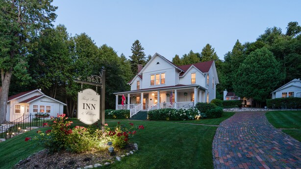 Une maison blanche à deux étages, dotée d’un porche, d’une enseigne indiquant « Auberge et gîte », et d’un chemin en briques menant à l’entrée.