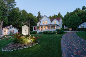 Une maison blanche à deux étages, dotée d’un porche, d’une enseigne indiquant « Auberge et gîte », et d’un chemin en briques menant à l’entrée.