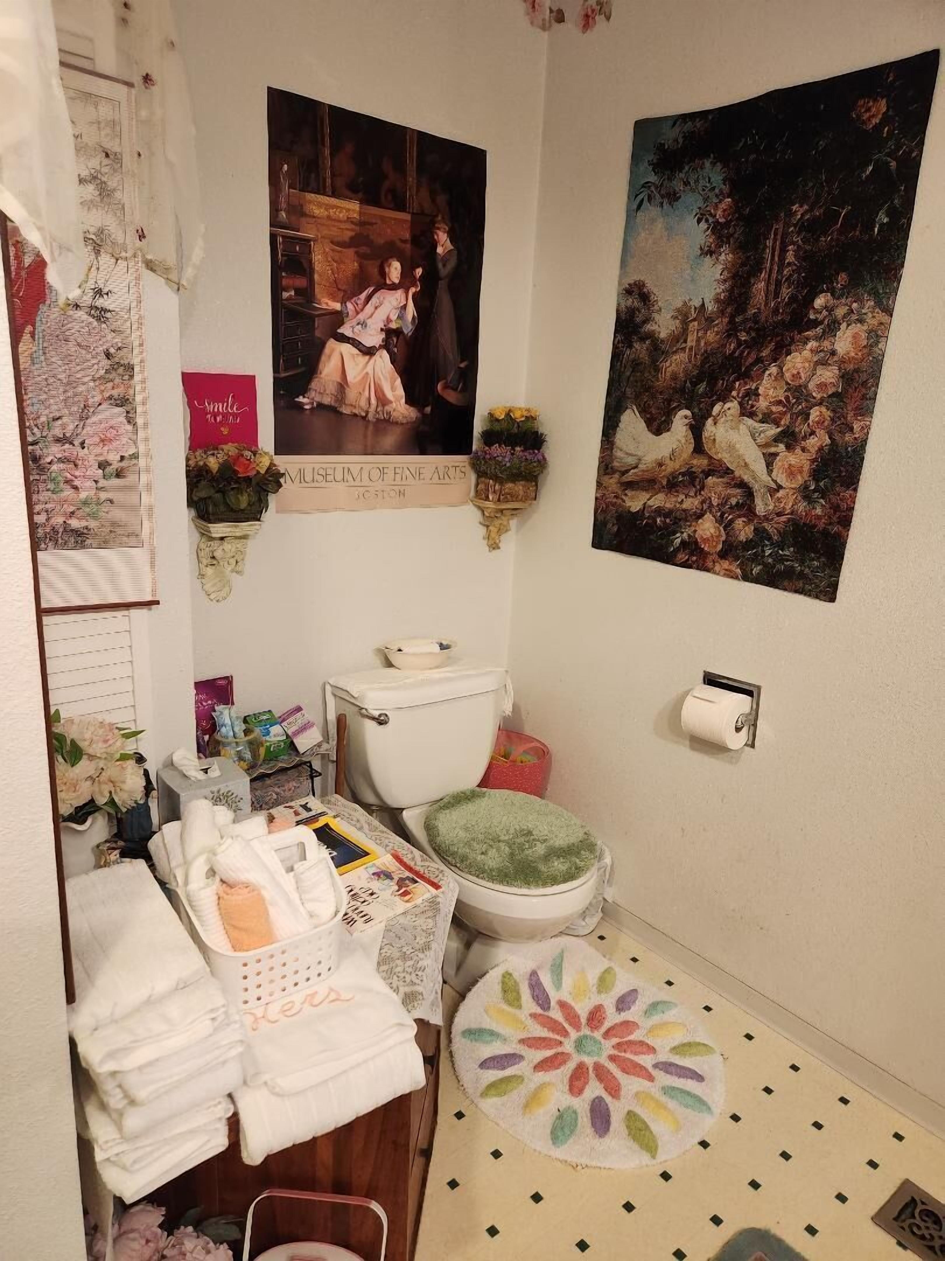 A bathroom with a toilet, a sink, a mirror, and a shower area. There are towels and toiletries on the counter.