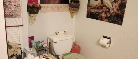 A bathroom with a toilet, a sink, a mirror, and a shower area. There are towels and toiletries on the counter.