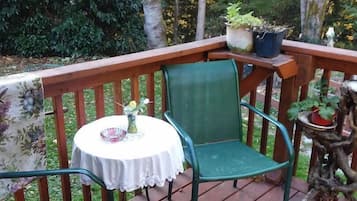 Relax on the deck surrounded by lush greenery, with a small table and two chairs.