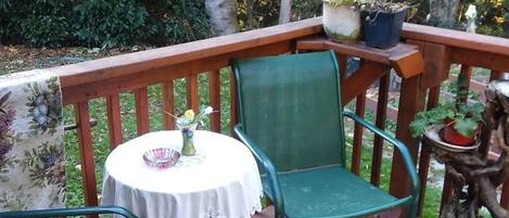 A wooden deck with a round table and two chairs, surrounded by greenery and trees.