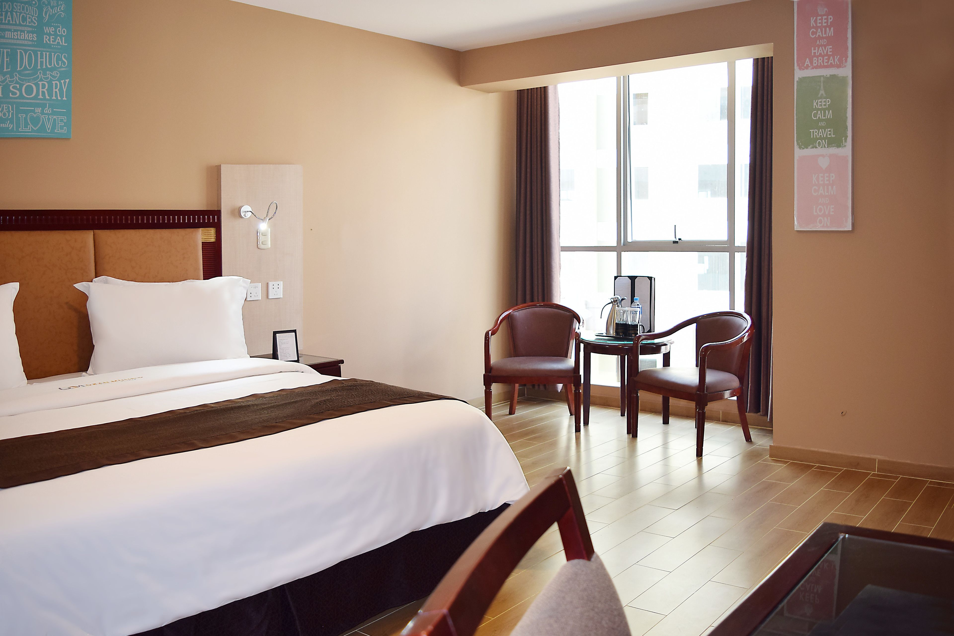 A hotel room with a large bed, a desk, two chairs, and a window with curtains.