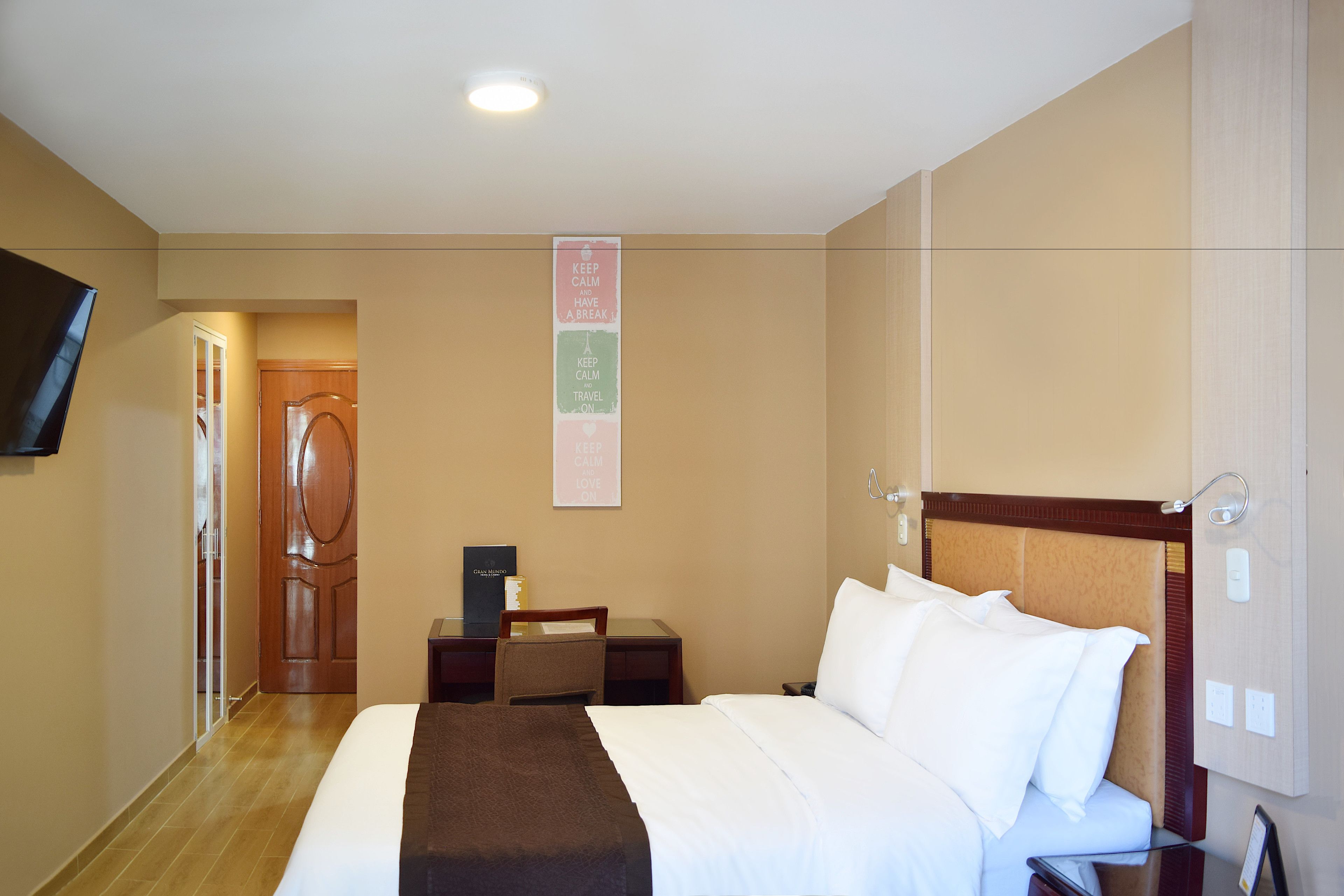 A hotel room with a bed, a desk, a chair, a TV, and a door.