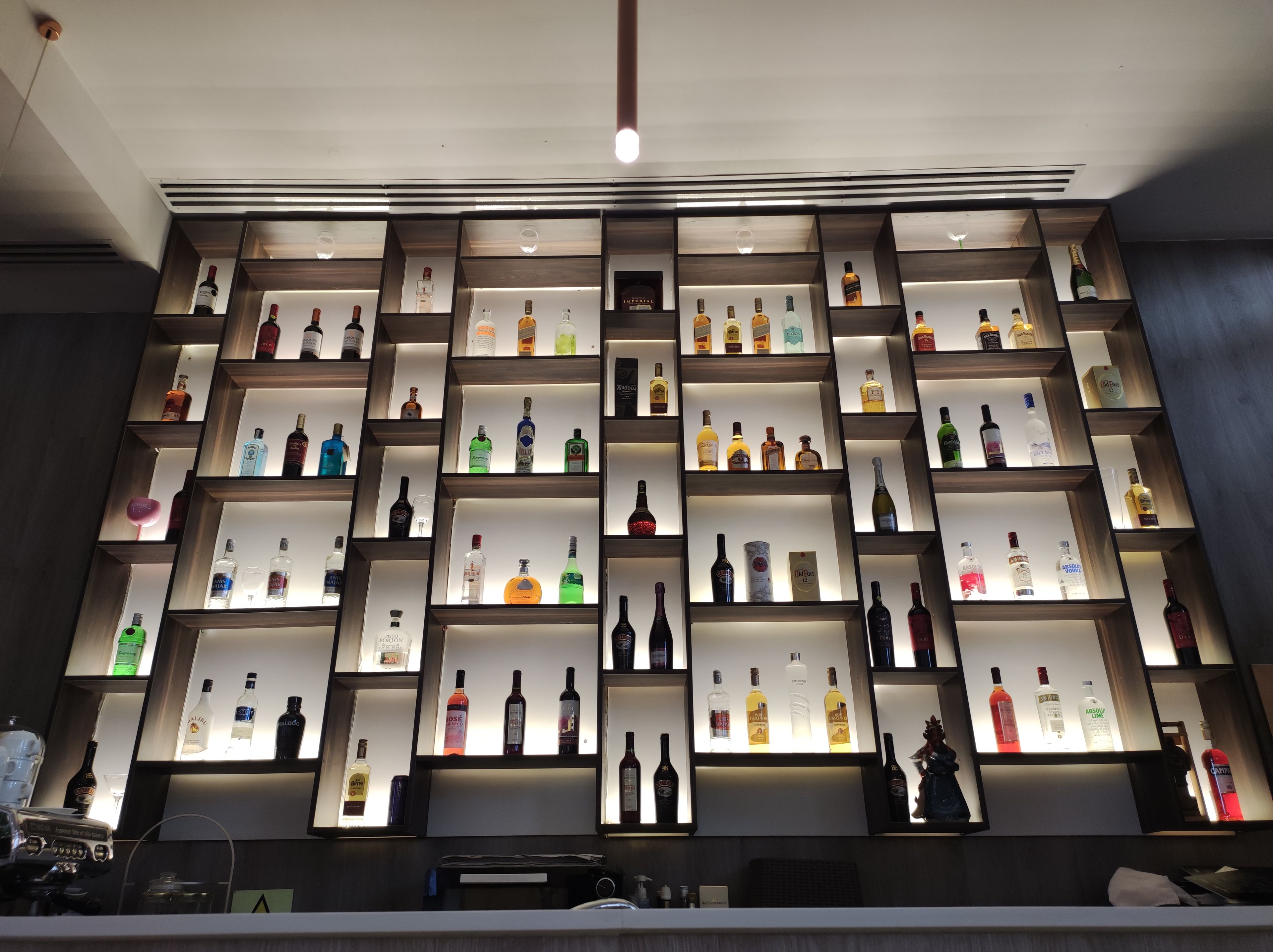 Un mur rempli d’étagères où sont exposées différentes bouteilles d’alcool, probablement dans un bar ou un magasin de boissons alcoolisées.