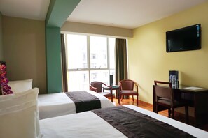 Habitación de hotel con dos camas, un escritorio, una silla, un televisor y una ventana con cortinas.
