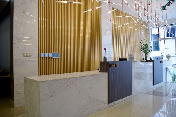 Un mostrador de recepción con encimera de mármol, un panel de pared de madera vertical y una lámpara moderna.
