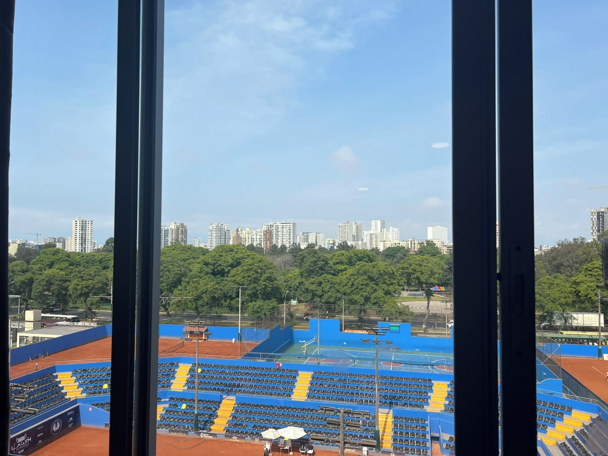 Una cancha de tenis con asientos y un paisaje urbano al fondo.