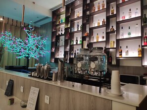 Eine Bar mit Regalen voller Spirituosenflaschen, einem dekorativen Baum mit Lichterketten und einer Theke mit Speisekarte und Barutensilien.