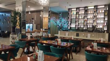 Ein Restaurant mit Holztischen und türkisfarbenen Stühlen, ein Barbereich mit Regalen voller Flaschen und dekorativer Beleuchtung.