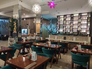 Restaurante com mesas de madeira e cadeiras azul-turquesa, área de bar com prateleiras de garrafas e iluminação decorativa.