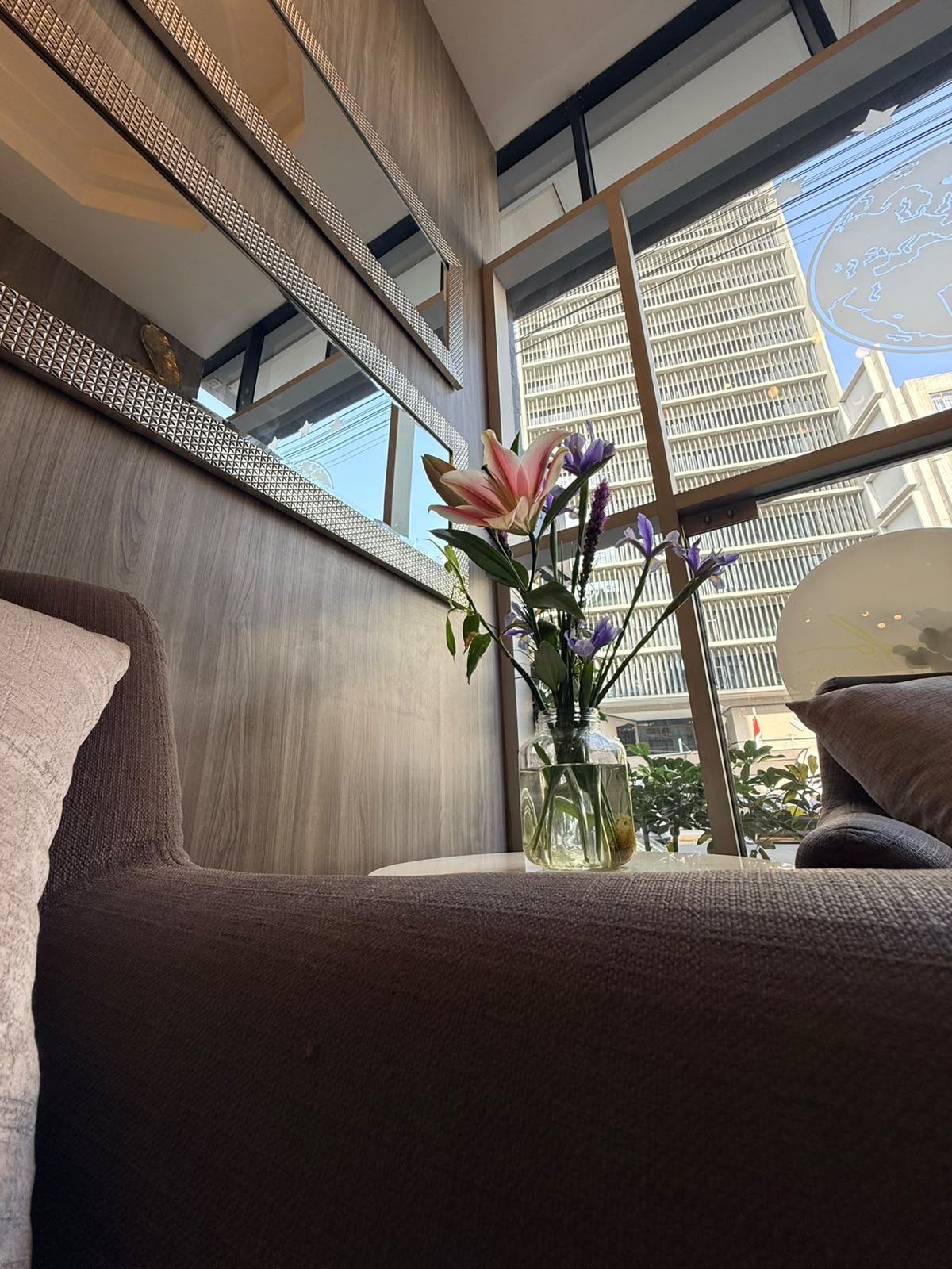 Un interior moderno con un ventanal grande, un florero con flores y un sofá.