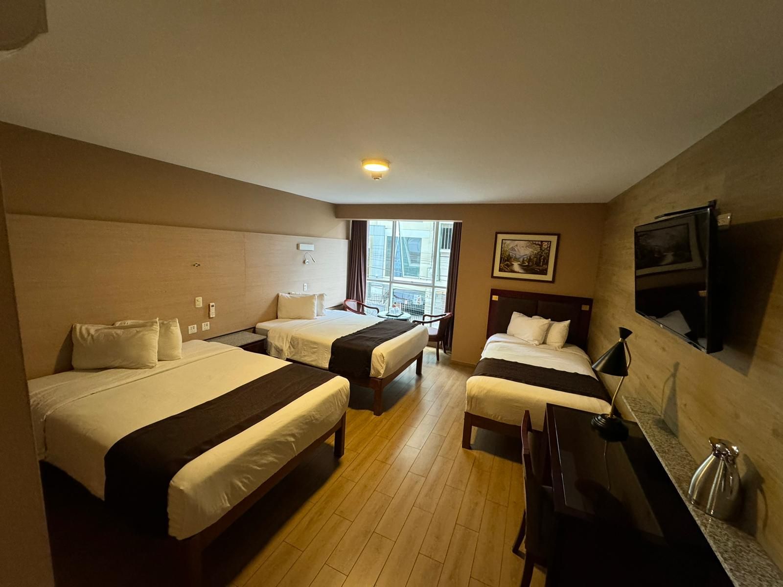 Habitación de hotel con dos camas, un televisor, un cuadro y una ventana con vistas.