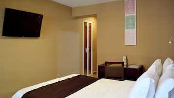 Hotelkamer met een bed, een flatscreen televisie aan de wand, een nachtkastje, een bureau en een deur naar een badkamer.