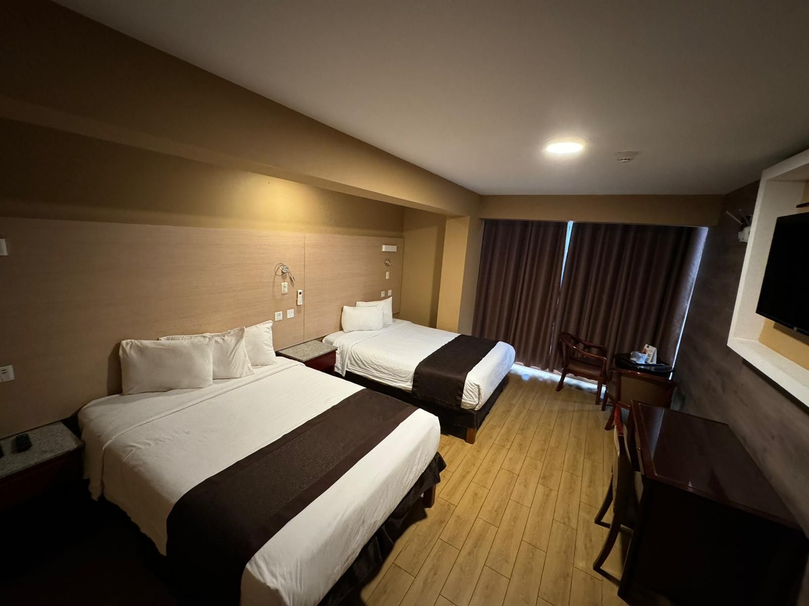 A hotel room with two beds, a desk, a chair, and a television.