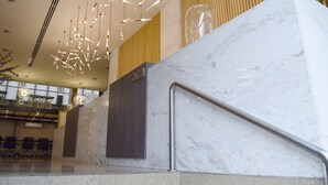 Un vestíbulo moderno con suelo de mármol, una escalera con barandilla de metal y lámparas colgantes.