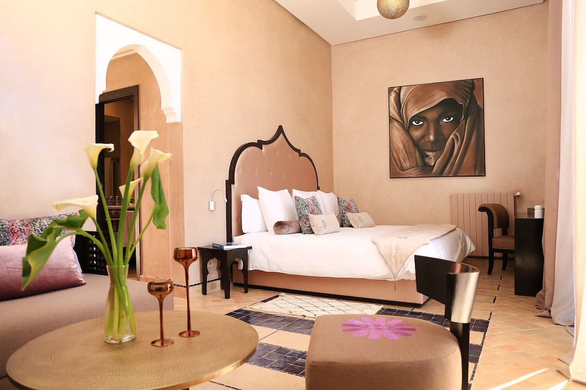 A bedroom with a bed, bedside table, chair, and a painting on the wall.