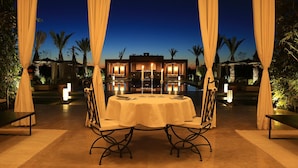 An outdoor dining area with a round table and chairs, surrounded by draped curtains, and illuminated by ambient lighting. - Dar Sofil - Adults Only (Marrakech)
