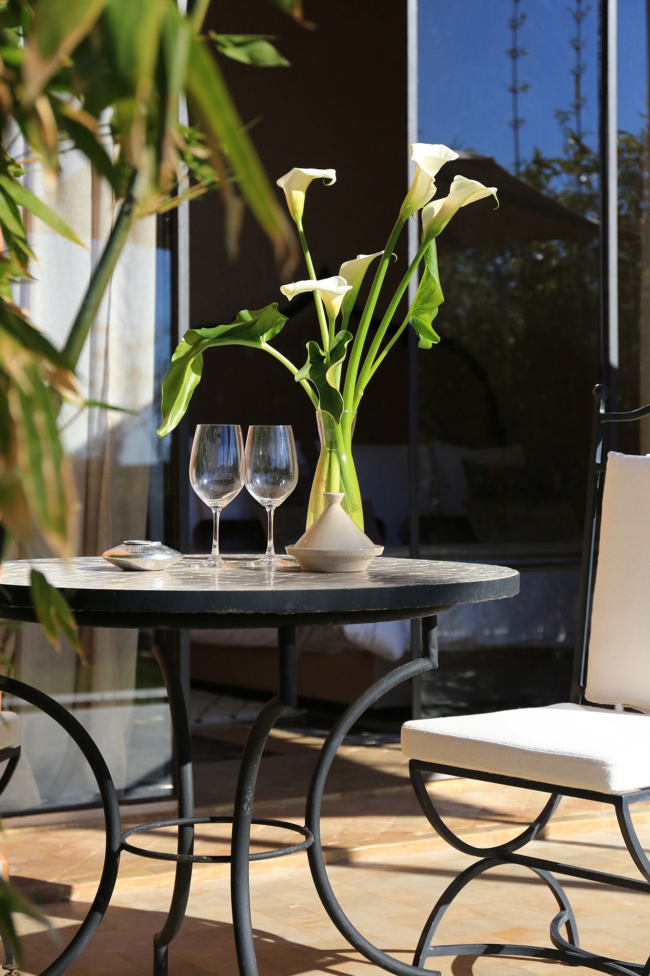 A table with two wine glasses, a vase with white flowers, and a chair.
