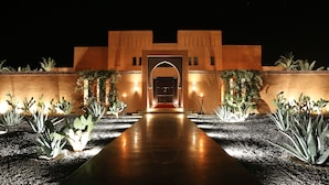 A building with a central archway, surrounded by cacti and illuminated by wall-mounted lights. - Dar Sofil - Adults Only (Marrakech)