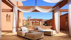 An outdoor seating area with a sofa and a table, draped with white fabric, set against a backdrop of a building with arches and a clear blue sky. - Dar Sofil - Adults Only (Marrakech)