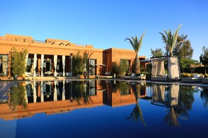 Un hotel con piscina que refleja el edificio y palmeras.