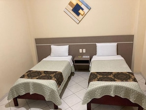 Habitación de hotel con dos camas individuales, una mesita de noche y una lámpara fijada a la pared.