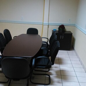 Un salón de conferencias con una mesa rectangular, seis sillas, un archivador pequeño y una planta en maceta.