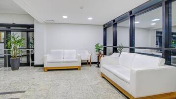 Un área de espera moderna con dos sofás blancos, una mesita y plantas en macetas.