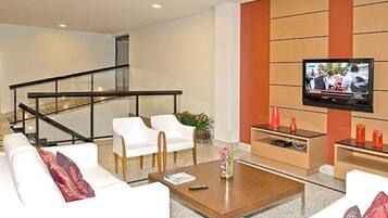 Una sala de estar moderna con un televisor de pantalla plana, sofás blancos, una mesa de centro y una escalera.