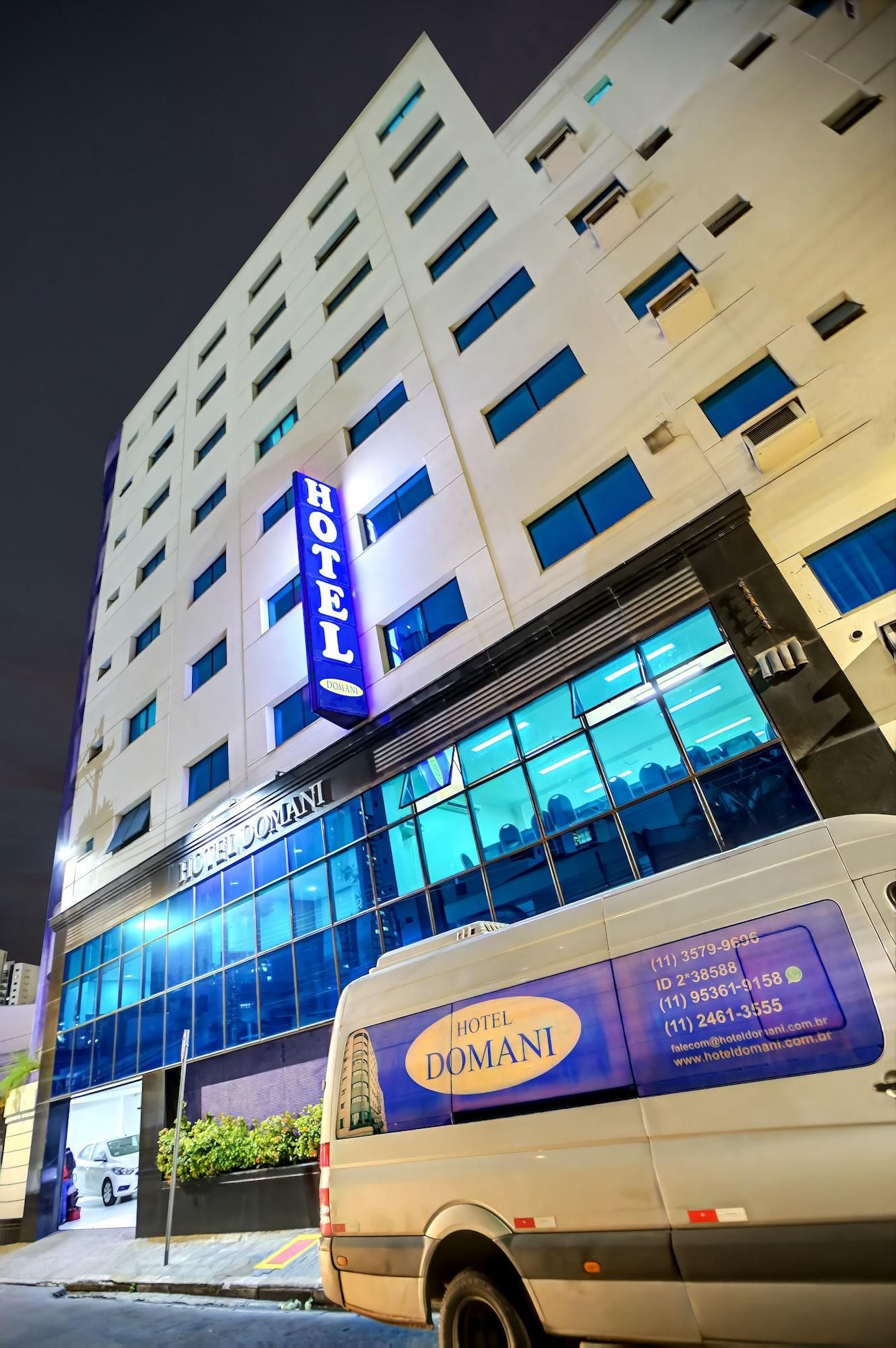 Un edificio de hotel con un letrero llamativo, amplias ventanas y una furgoneta estacionada frente a él.